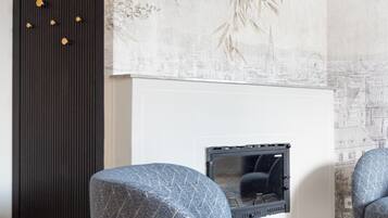 A modern living room with a fireplace, two patterned armchairs, a dark accent wall, and a cityscape mural.