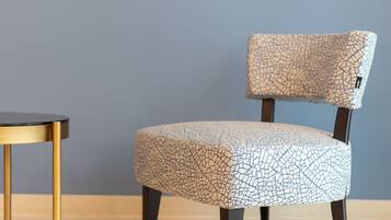 A chair with a cracked pattern upholstery, a round table with a gold frame, and a plain wall.