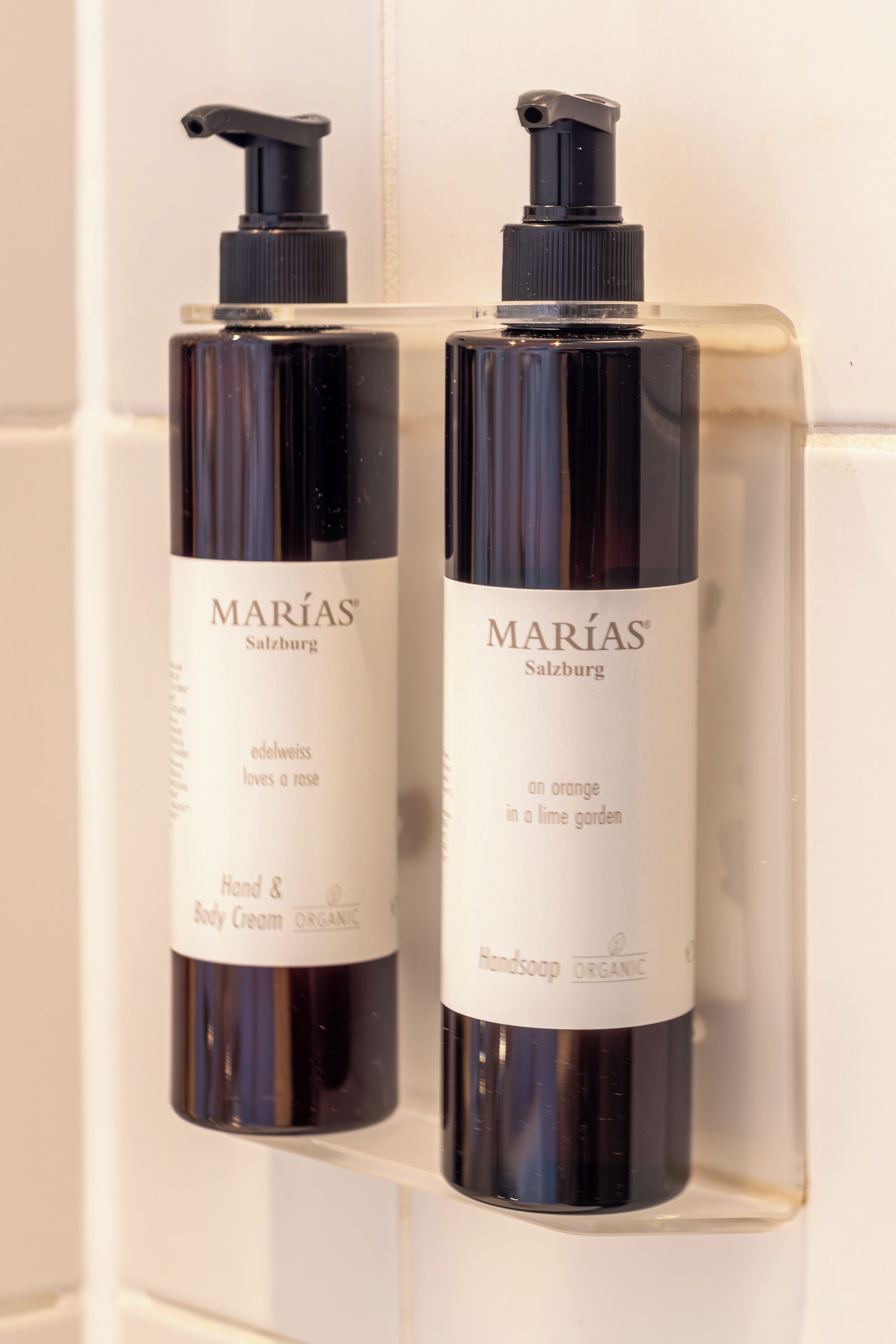 Twee flessen Marías Salzburg body lotion en handzeep op een witte betegelde muur.