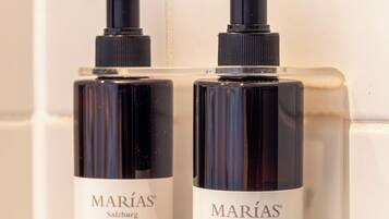 Twee flessen Marías Salzburg body lotion en handzeep op een witte betegelde muur.