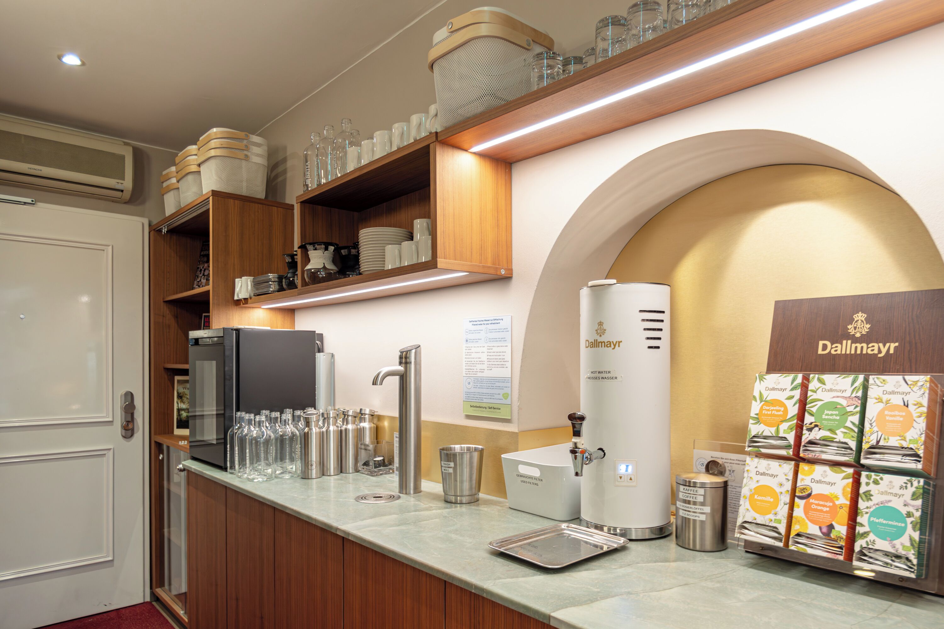 Una cocina de hotel con una cafetera, dispensador de agua y una variedad de sobres de café.