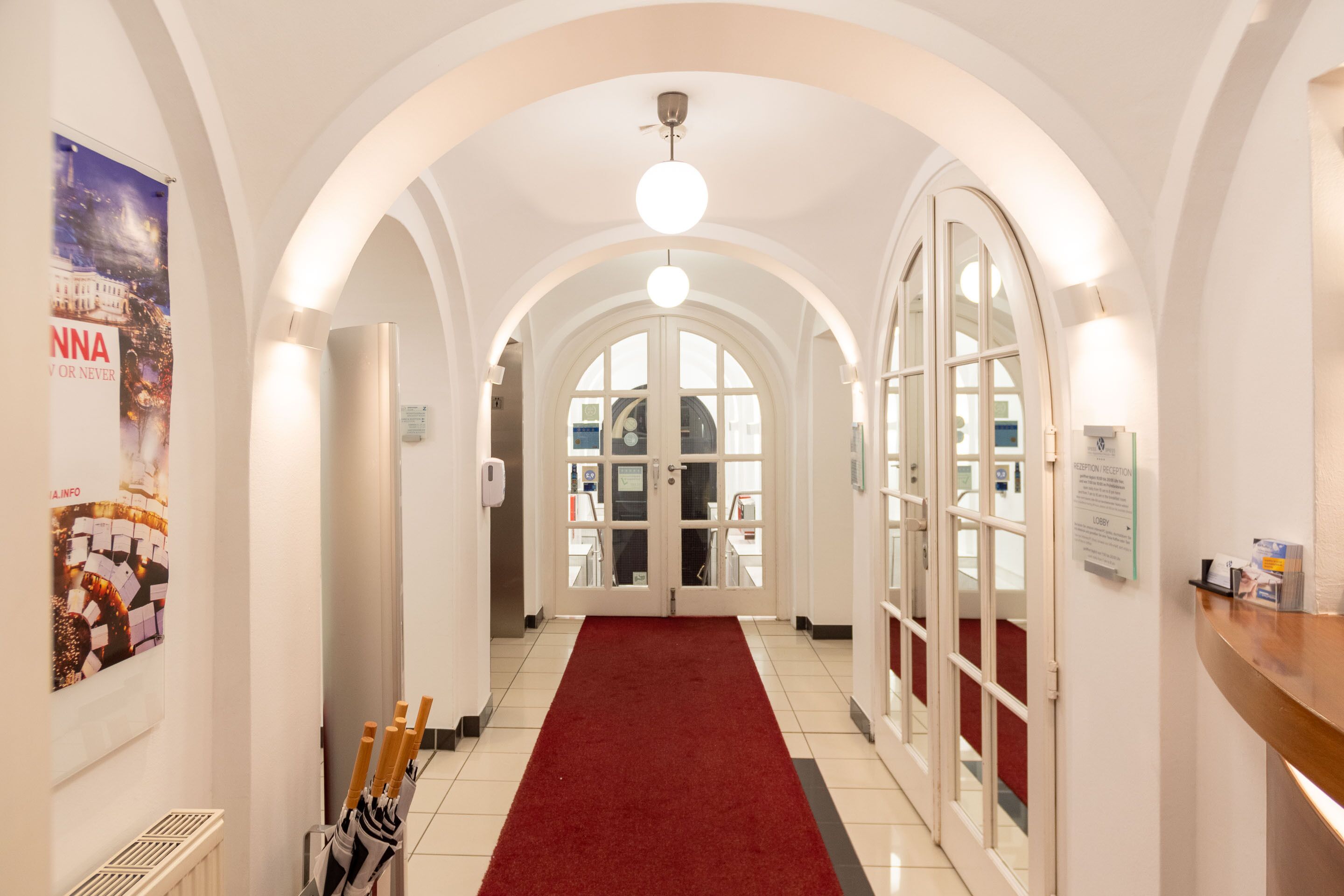 A hotel corridor with white walls, a red carpet, and arched ceilings.