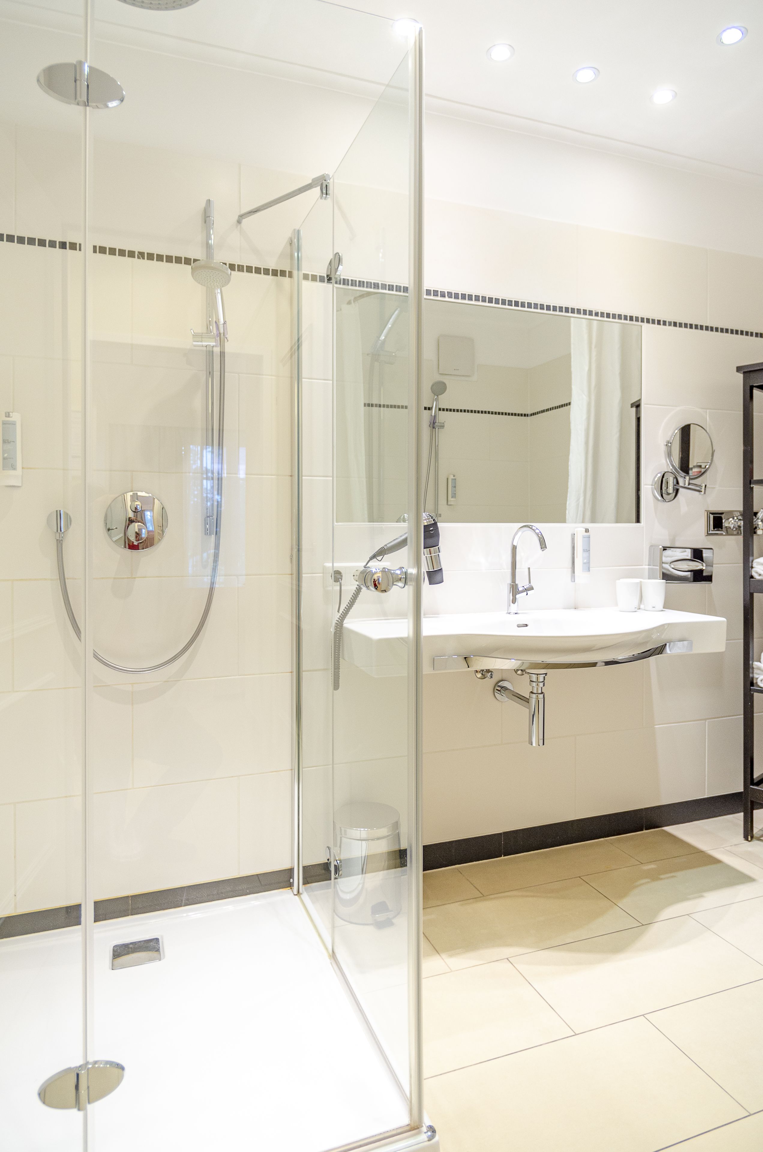 A modern bathroom with a glass-enclosed shower, a white sink, and a large mirror.