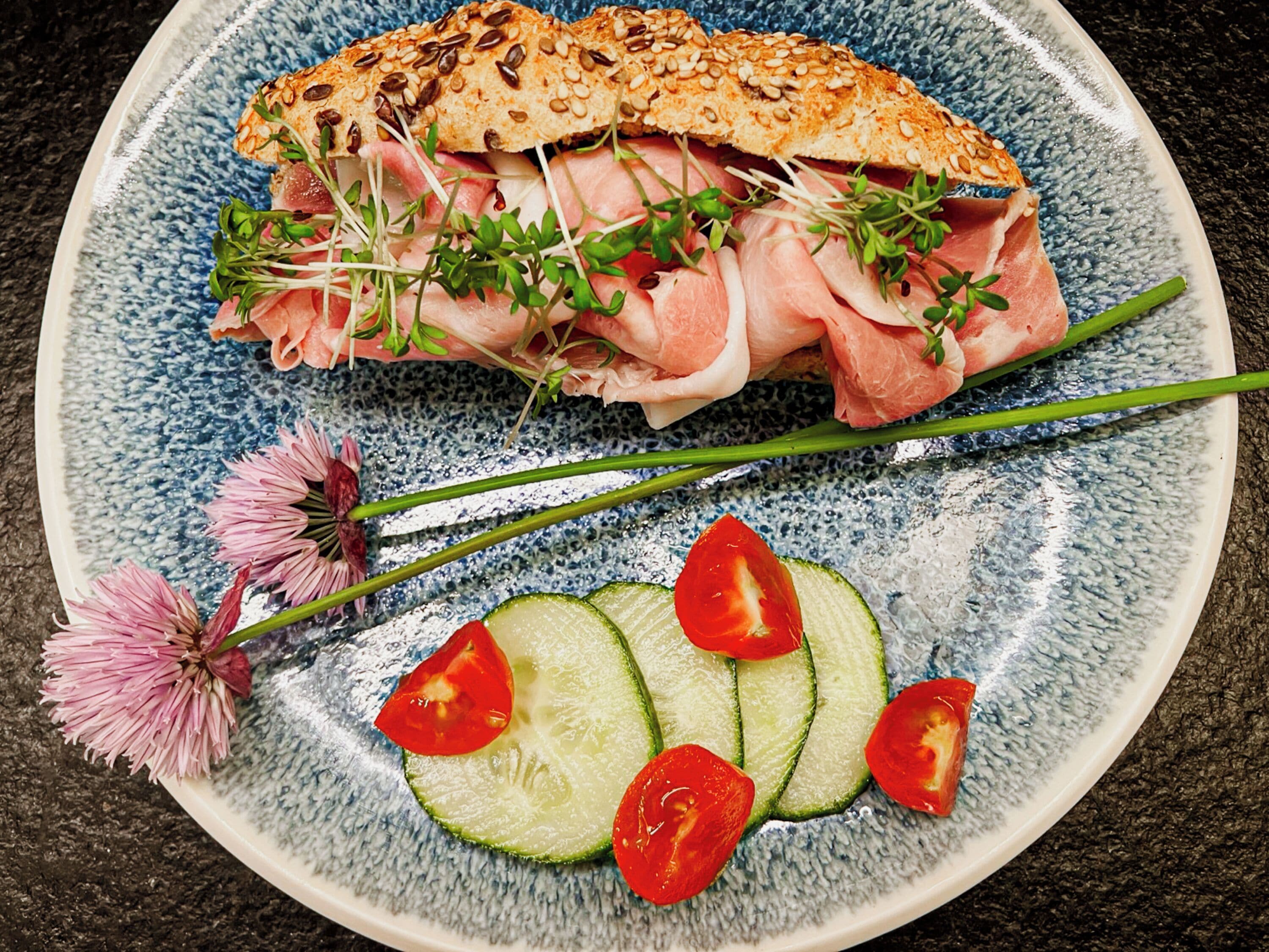 Un plat amb un entrepà, rodanxes de pepino i una flor.