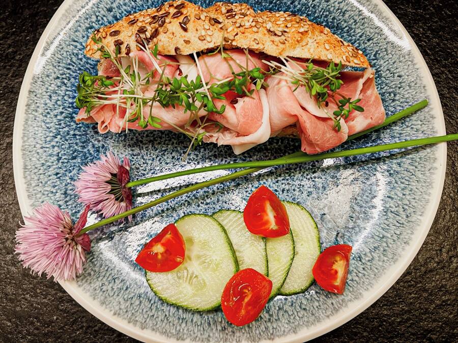 Un plat amb un entrepà, rodanxes de pepino i una flor.