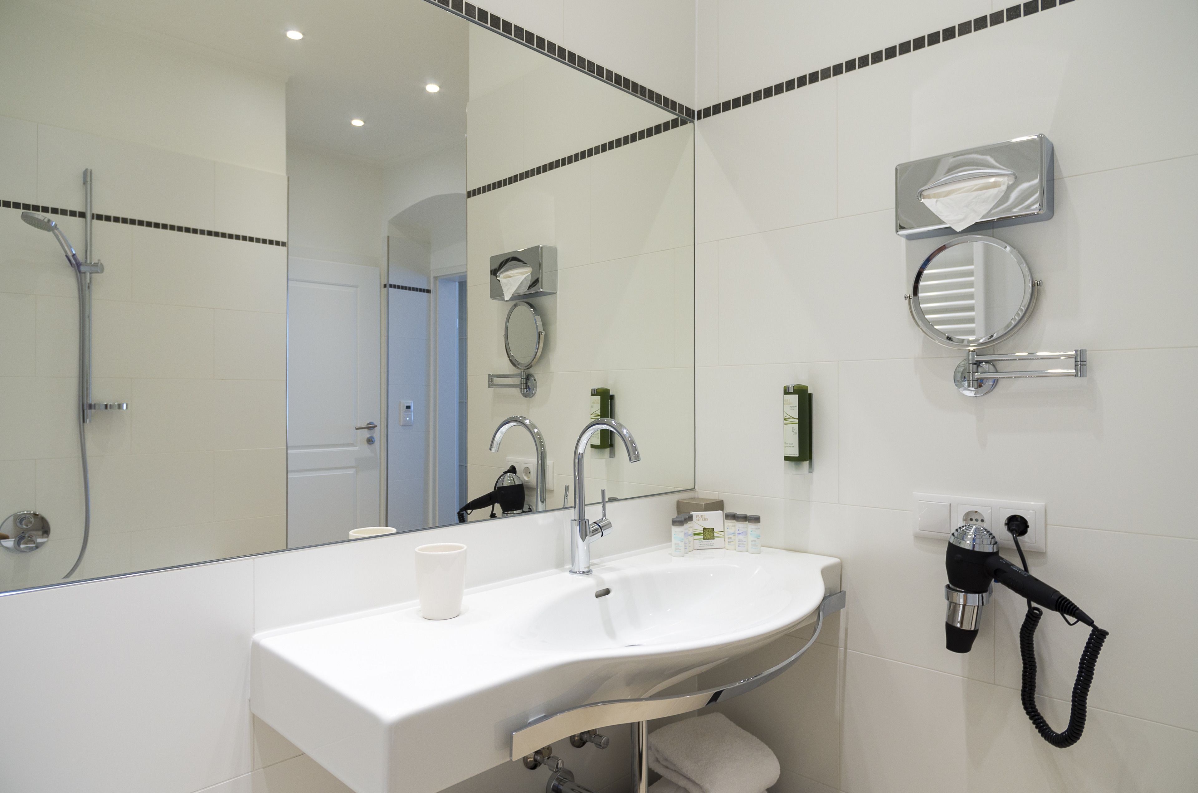 Ein modernes Badezimmer mit einem großen Spiegel, einem Waschbecken, einer Handbrause und einem Handtuchhalter.