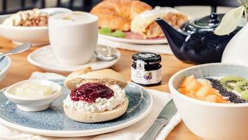 En frukostuppsättning med en croissant, en kopp kaffe, en skål med frukt och en tekanna på ett träbord.