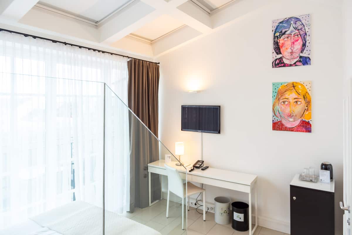 A hotel room with a desk, chair, and a television on the wall.
