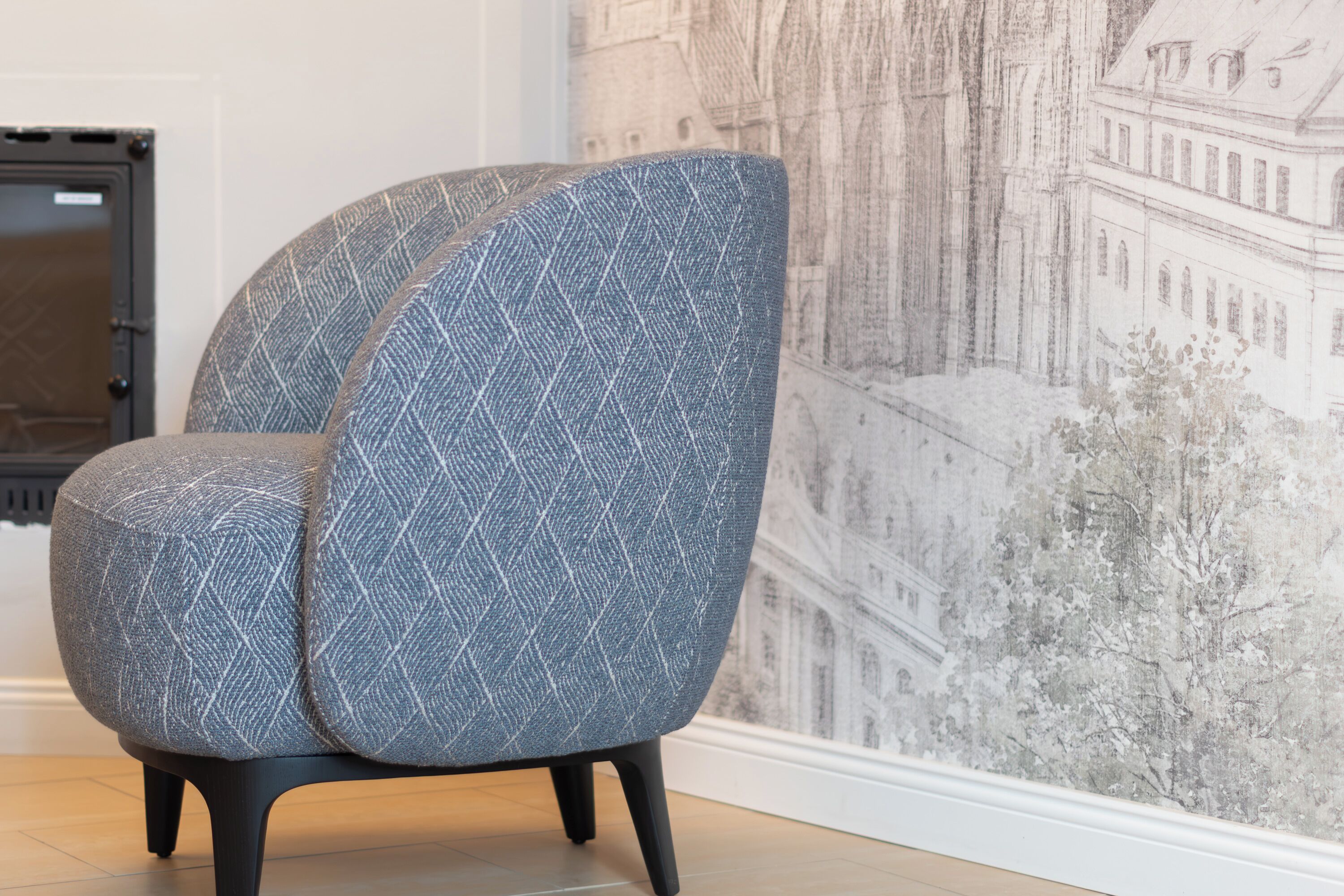 A modern chair with a geometric pattern, positioned in a room with a large, detailed mural on the wall.