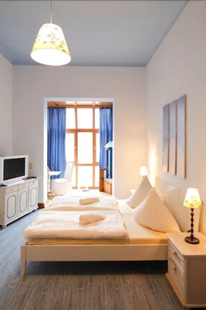 Un dormitorio con cama, televisor, lámpara y ventana con cortinas.