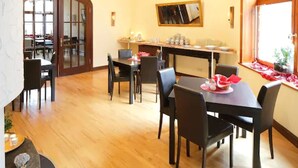 Een eetruimte met een houten vloer, zwarte stoelen en een tafel gedekt met rode servetten en borden.