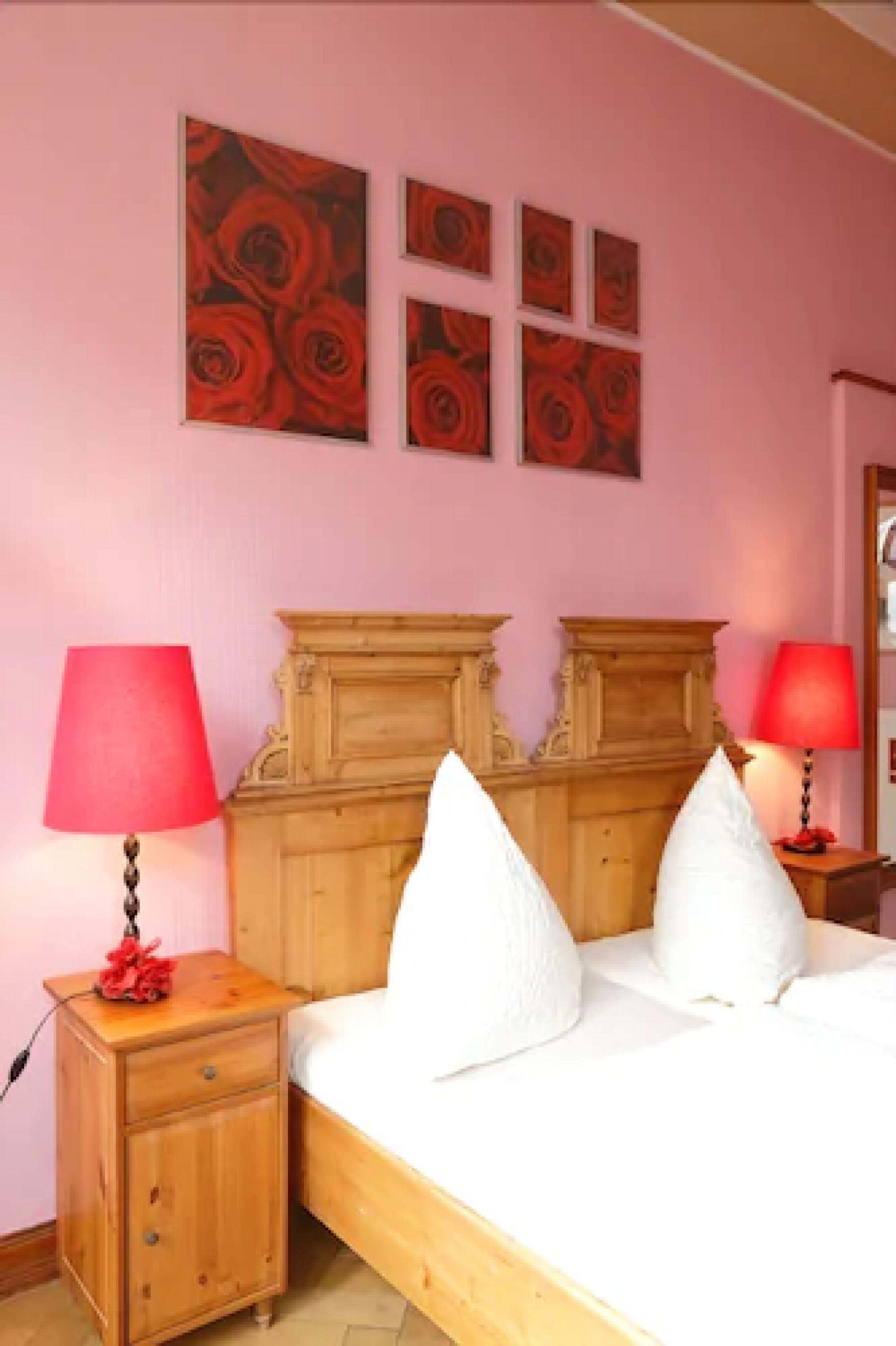 A bedroom with a wooden bed, two bedside tables with lamps, and four framed pictures on the wall.