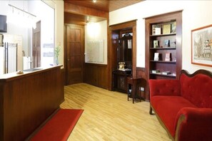Un mostrador de recepción de madera, un sofá rojo y una estantería en una habitación con suelo y paredes de madera.