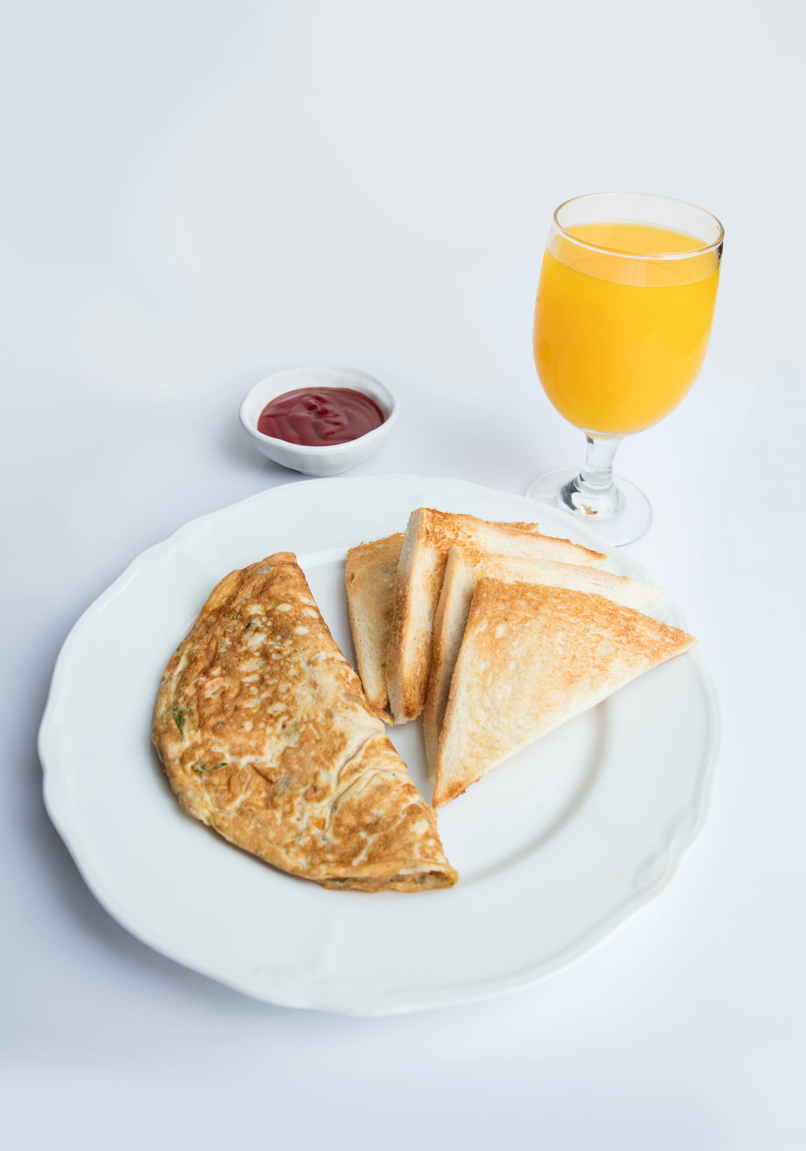 Un plato con una tortilla enrollada, un vaso de zumo de naranja y un recipiente pequeño con kétchup.