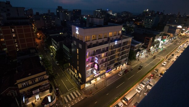 A multi-story hotel with illuminated signage, a street view, and a cityscape in the background.