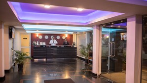 A hotel reception area with a modern design, featuring a reception desk, a clock, and a glass door leading to the lobby.