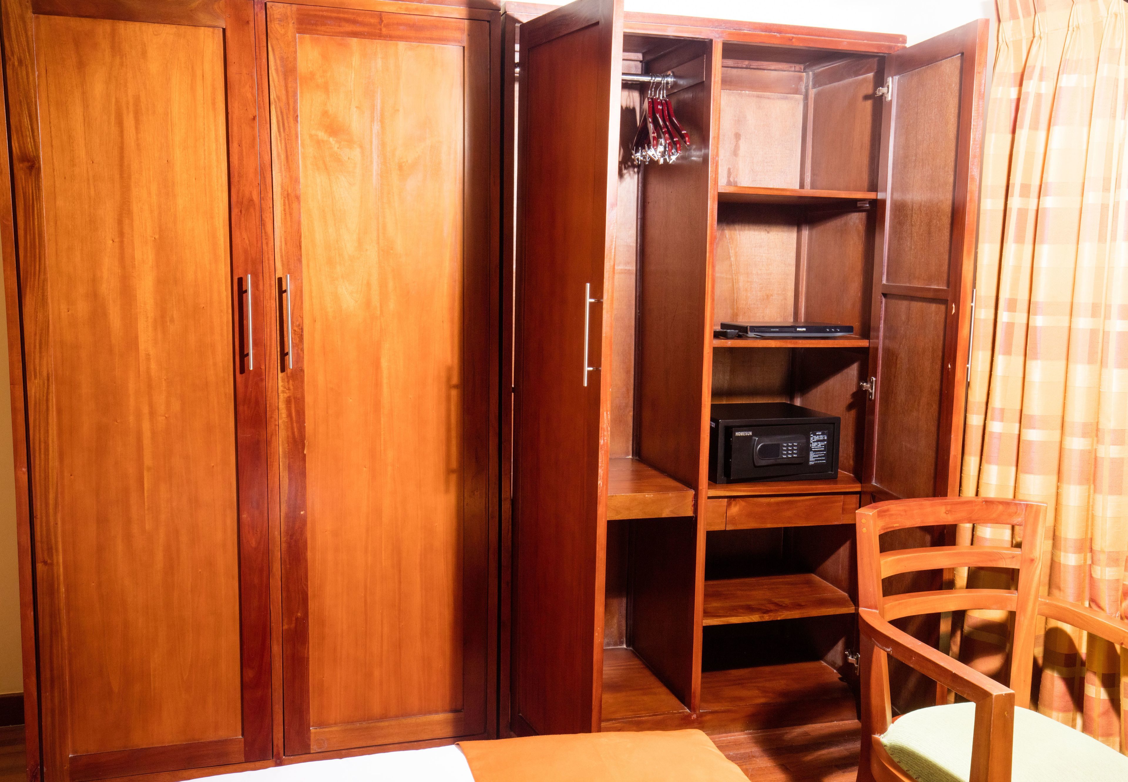 A wooden wardrobe with multiple compartments, a chair, and a shelf with a black electronic device.