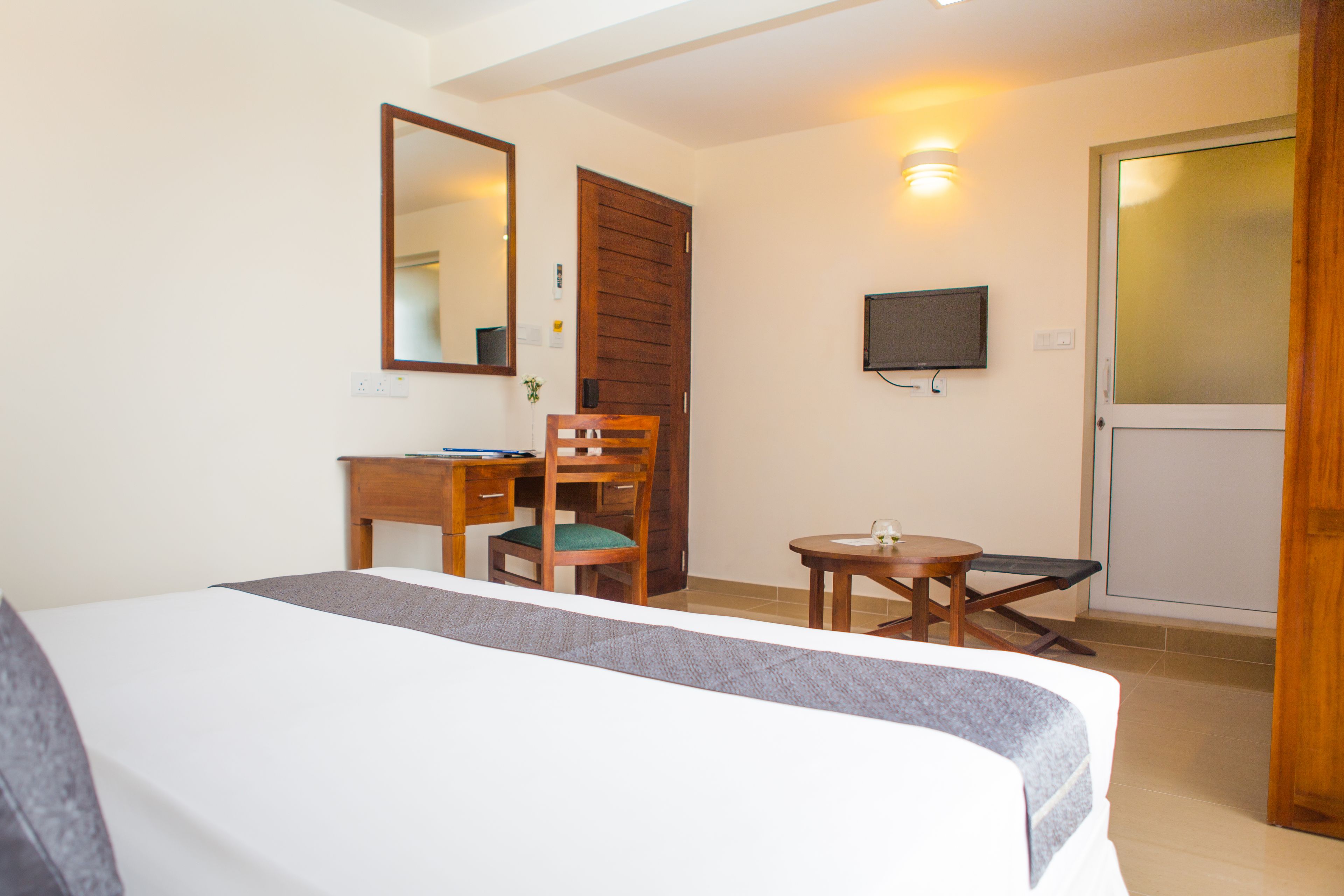Une chambre d’hôtel comprenant un lit, un bureau avec une chaise, une petite table, un téléviseur fixé au mur et une porte.