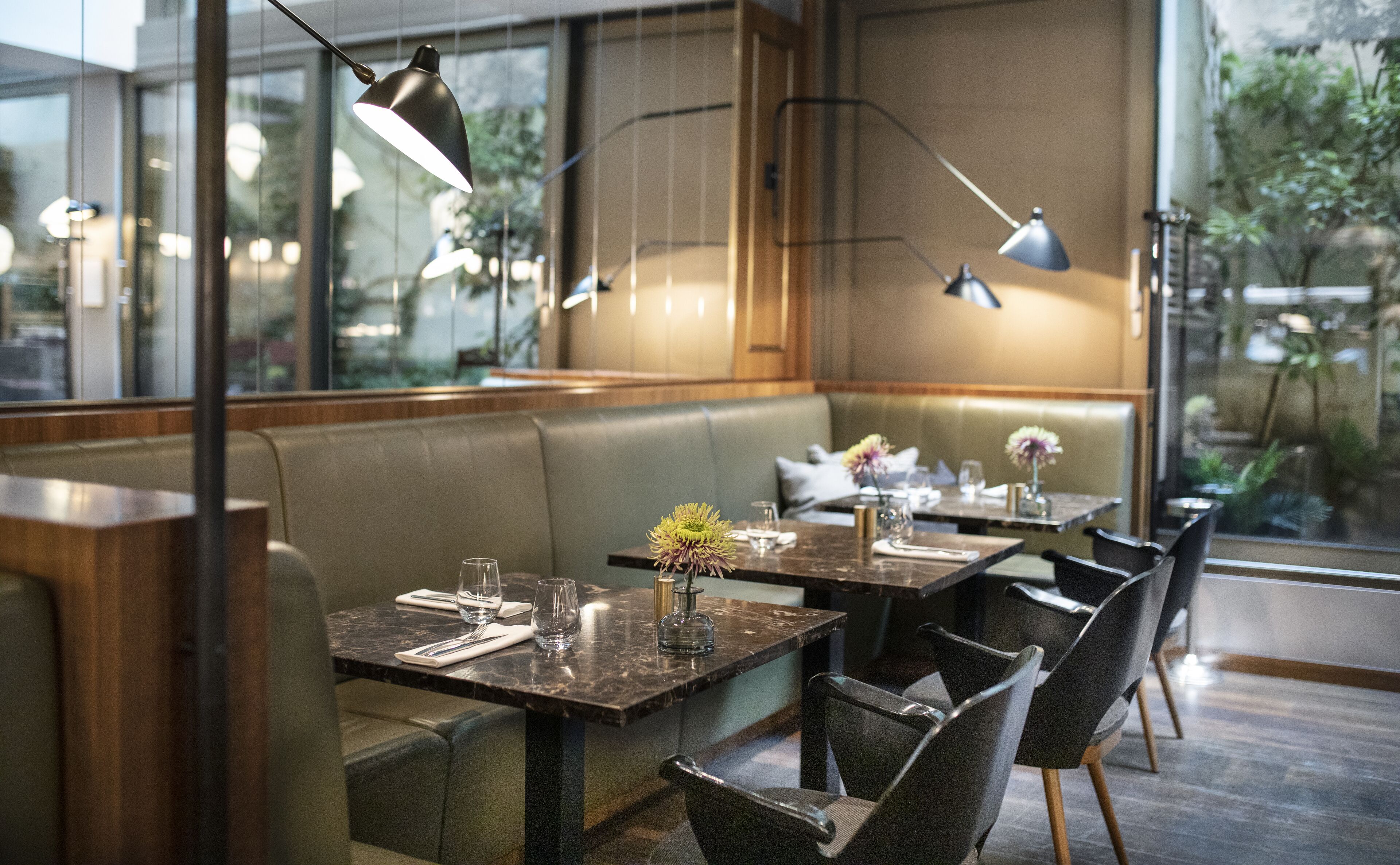 Een restaurantinterieur met zitbankjes, tafels en hangende lampen.