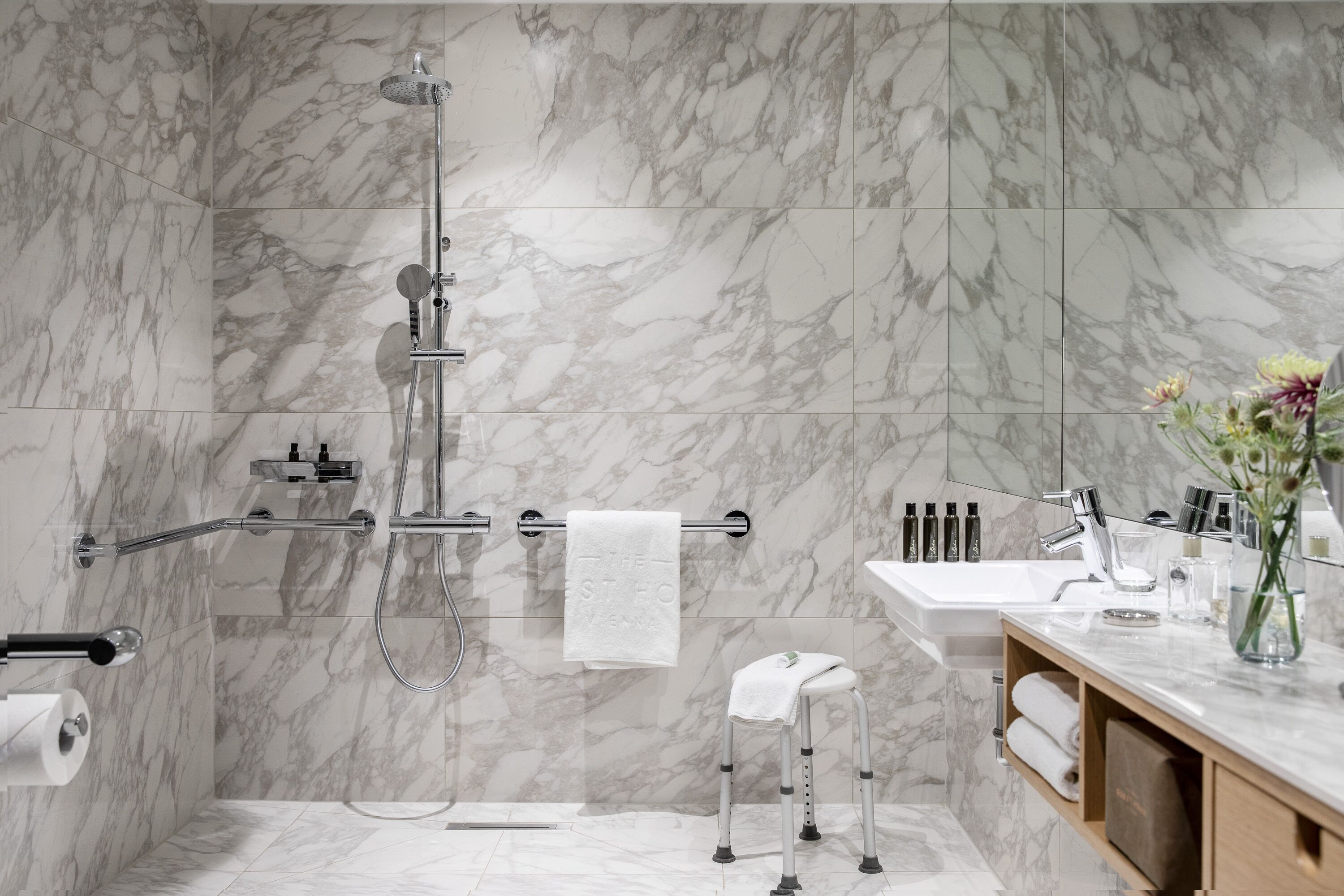 Uma casa de banho moderna com azulejos de mármore, chuveiro, sanita, lavatório e toucador com produtos de higiene pessoal.