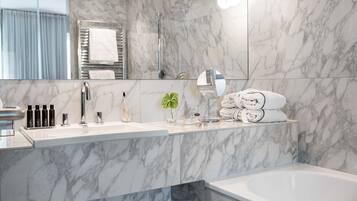Un baño moderno con paredes de mármol, una bañera grande, un tocador con espejo y un perchero para toallas.