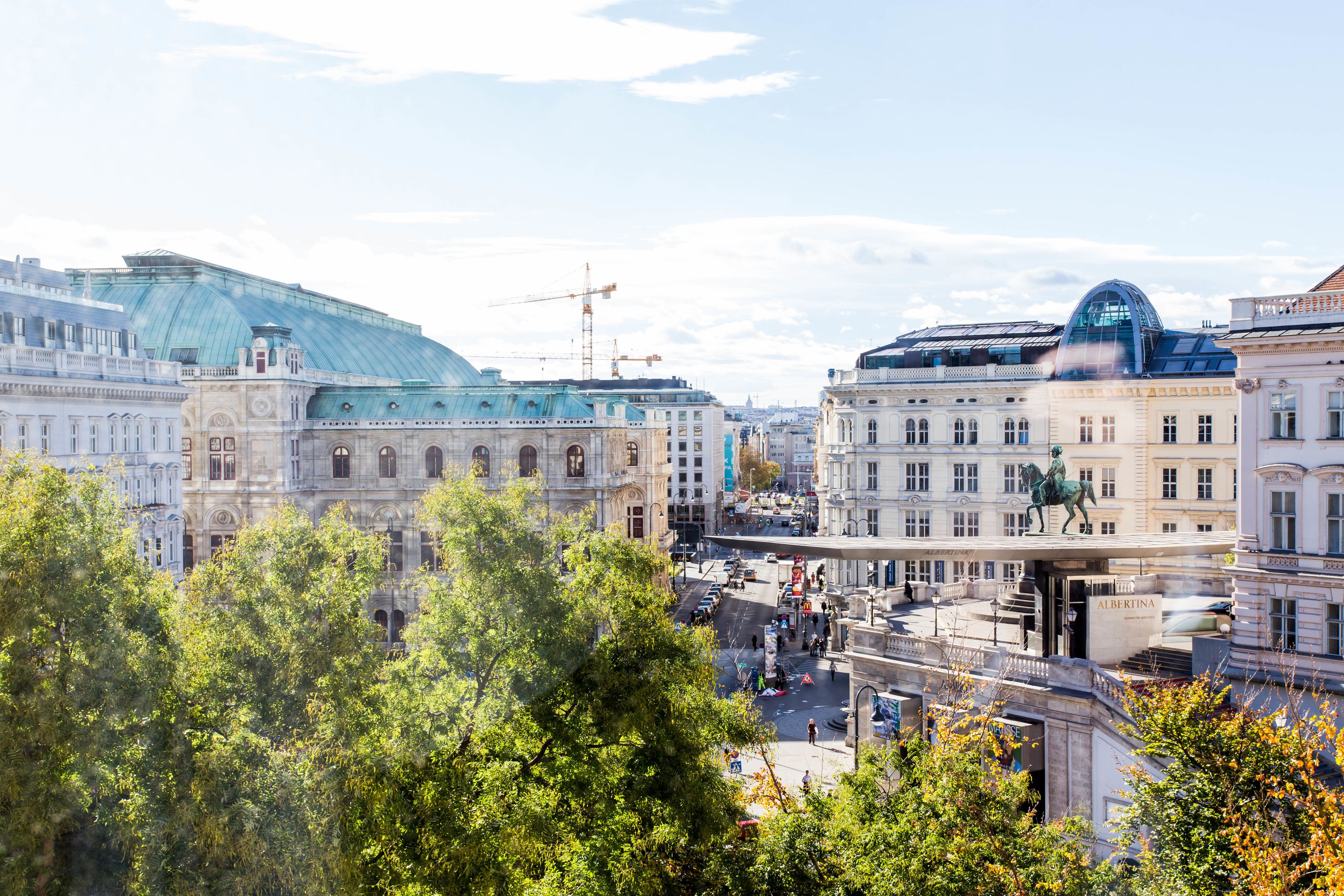 A cityscape with historic buildings, a prominent dome structure, and a statue on a pedestal.