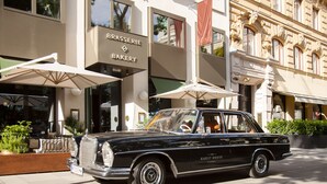 Un coche negro clásico estacionado frente a un edificio con un letrero que dice 'BRASSERIE BAKERY'.