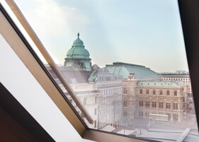 Vista dalla finestra su un paesaggio urbano con edifici storici e una cupola verde ben visibile.