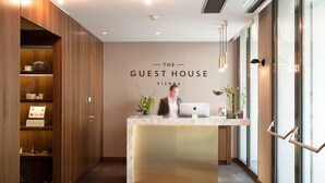 Un mostrador de recepción con un cartel que dice "The Guest House Vienna" en un interior moderno con paneles de madera y una encimera de mármol.