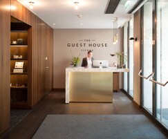 A reception desk with a sign reading "The Guest House Vienna" in a modern interior with wooden paneling and a marble counter.