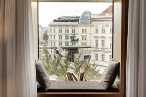 A view from a window with a cushioned bench, a statue, and a building with classical architecture.