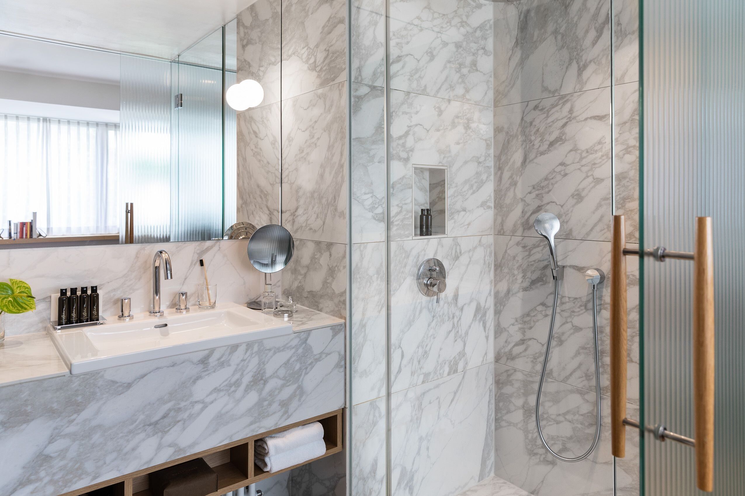 Un baño moderno con lavamanos de mármol, un espejo, un cabezal de ducha de mano y una ducha con mampara de vidrio.