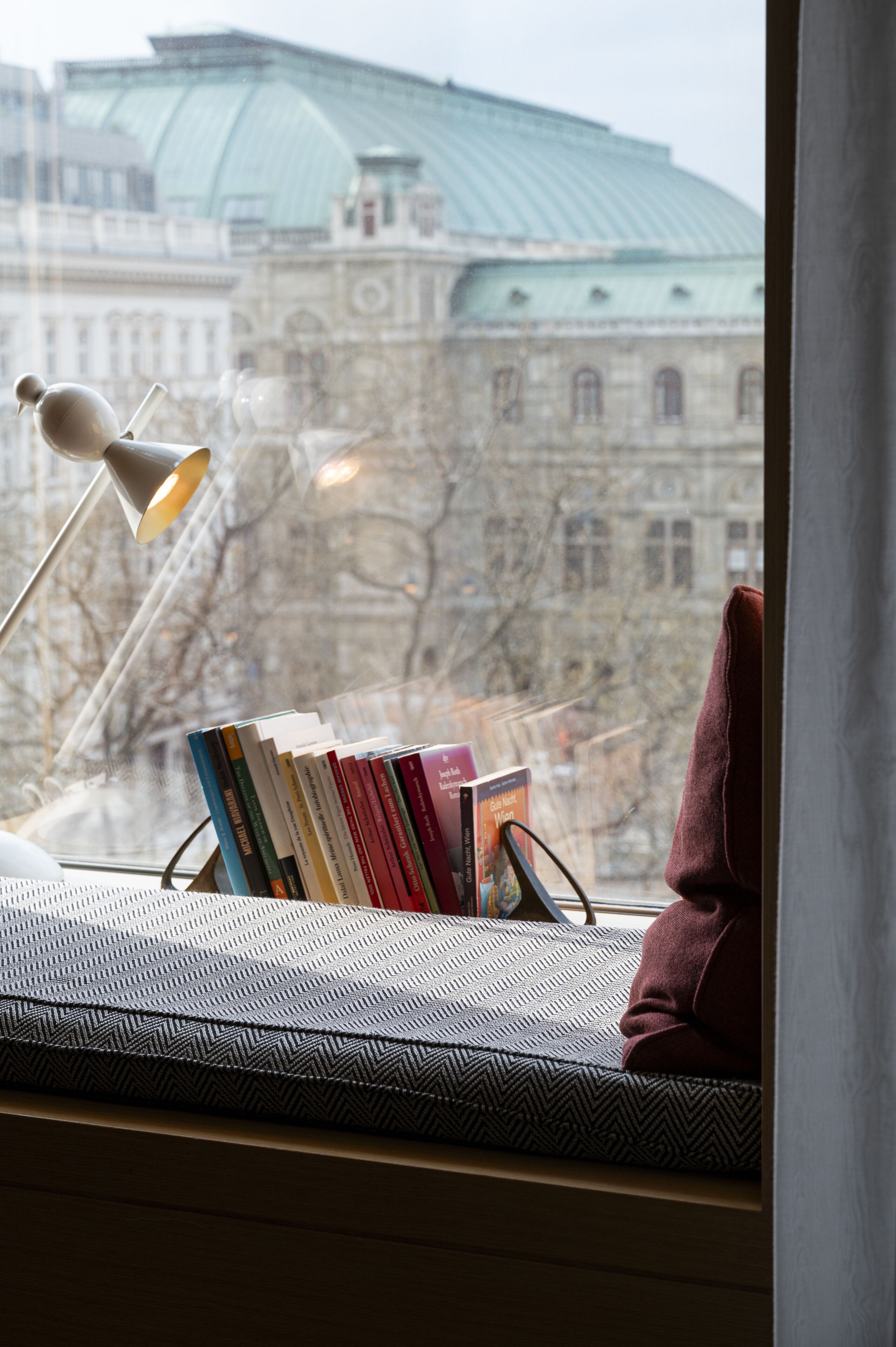 Assento junto à janela com uma luminária, livros e almofada.