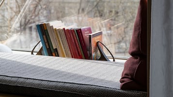Assento junto à janela com uma luminária, livros e almofada.