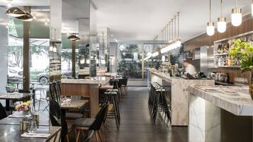 Interior moderno de restaurante com bancadas de mármore, cadeiras pretas e luminárias pendentes.
