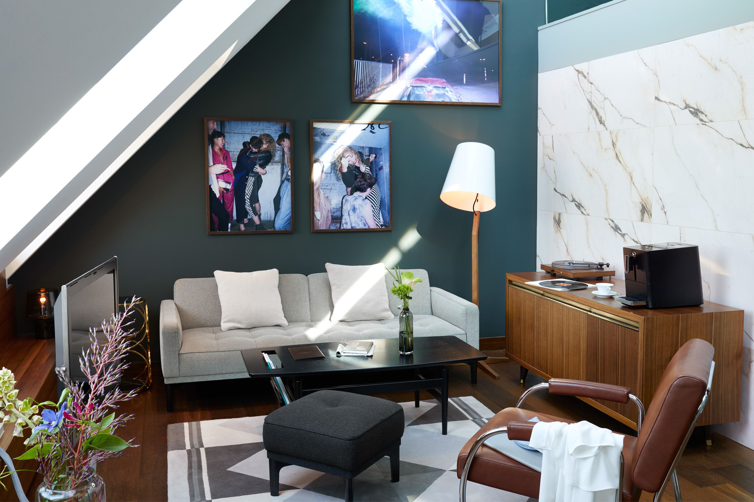 A modern living room with a sofa, coffee table, ottoman, and a desk with a lamp.