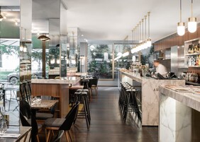 A modern restaurant with a long counter, bar stools, and a view of the street.
