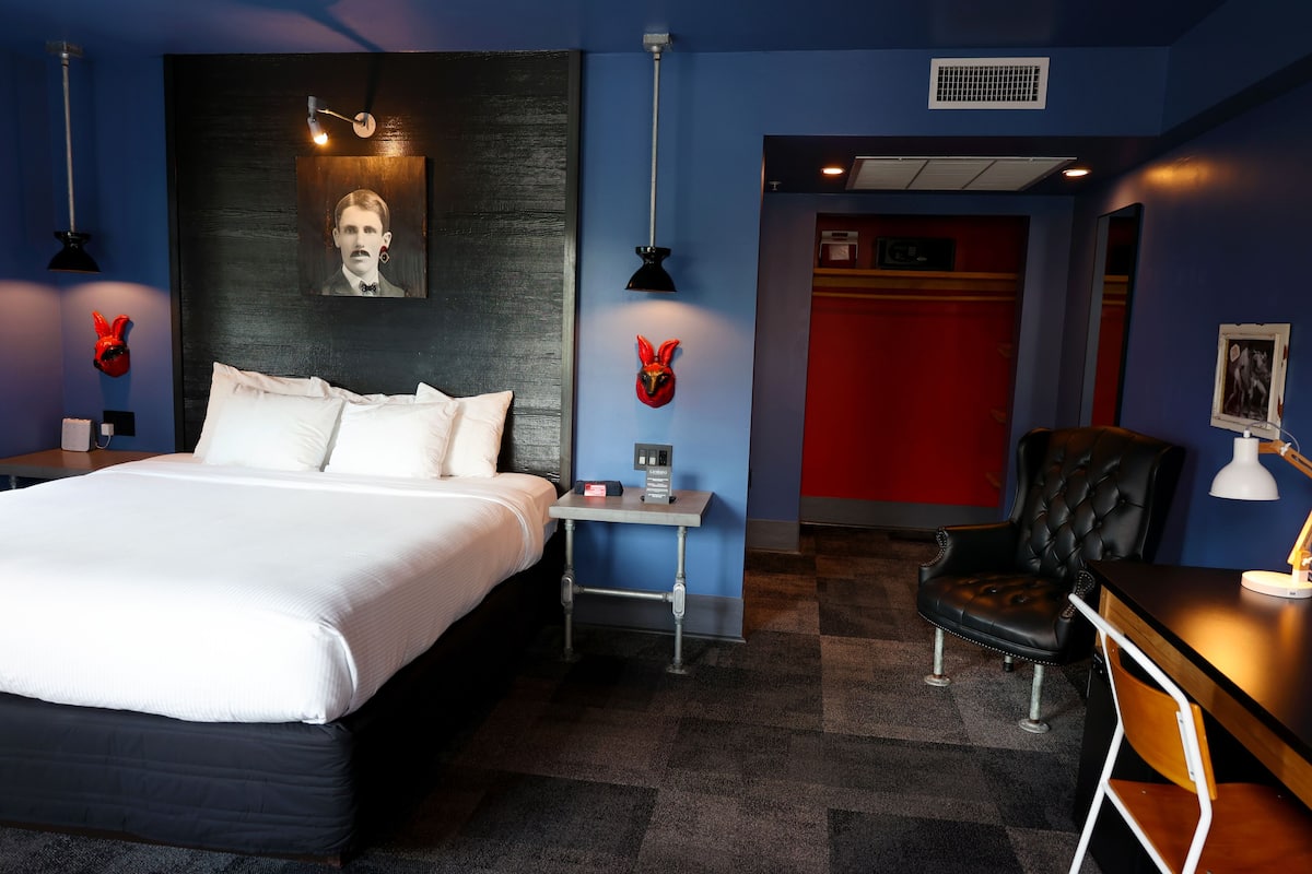 Une chambre d’hôtel avec un lit, une table de chevet, une lampe, une chaise et un mur d’accent rouge.