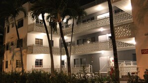 Een hotel met meerdere verdiepingen, balkons, palmbomen en een goed verlichte gevel.