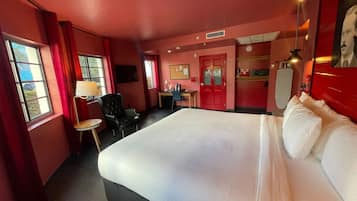 Quarto de hotel com uma cama grande, escrivaninha, cadeira e televisão.