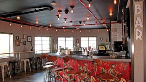 Een barruimte met bloemenbehang in rood, meerdere krukken en een bar met verschillende spullen.