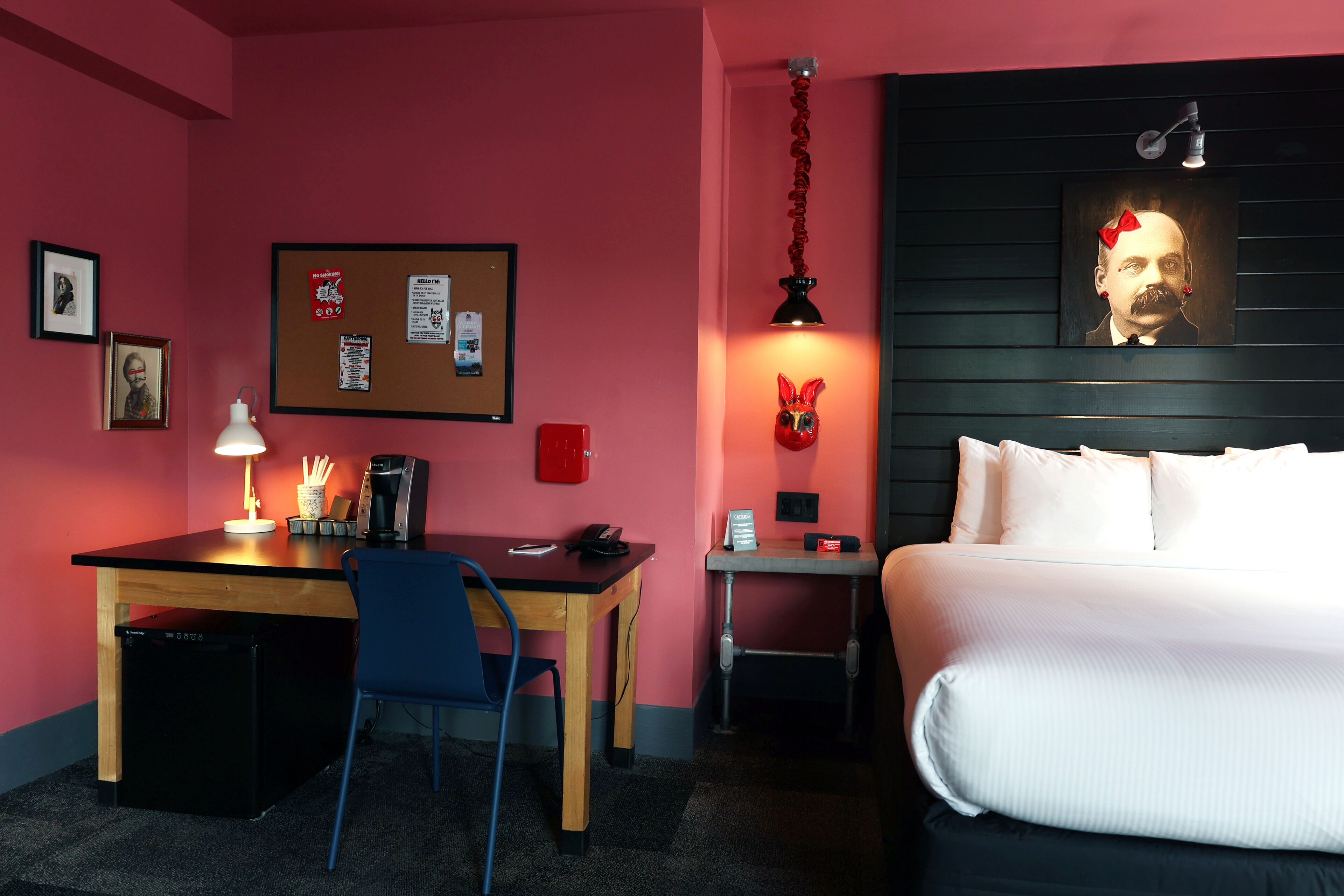 Ein Hotelzimmer mit Bett, Schreibtisch, Stuhl und einer Pinnwand an der Wand.