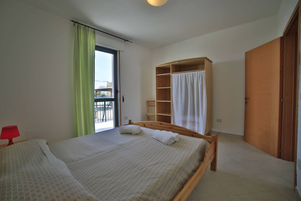 A bedroom with a bed, a wardrobe, a red lamp, and a view through a window.