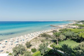 A beach with umbrellas and sun loungers, a clear blue sea, and a grassy area with trees. - Residence Cala Verde (Taviano)