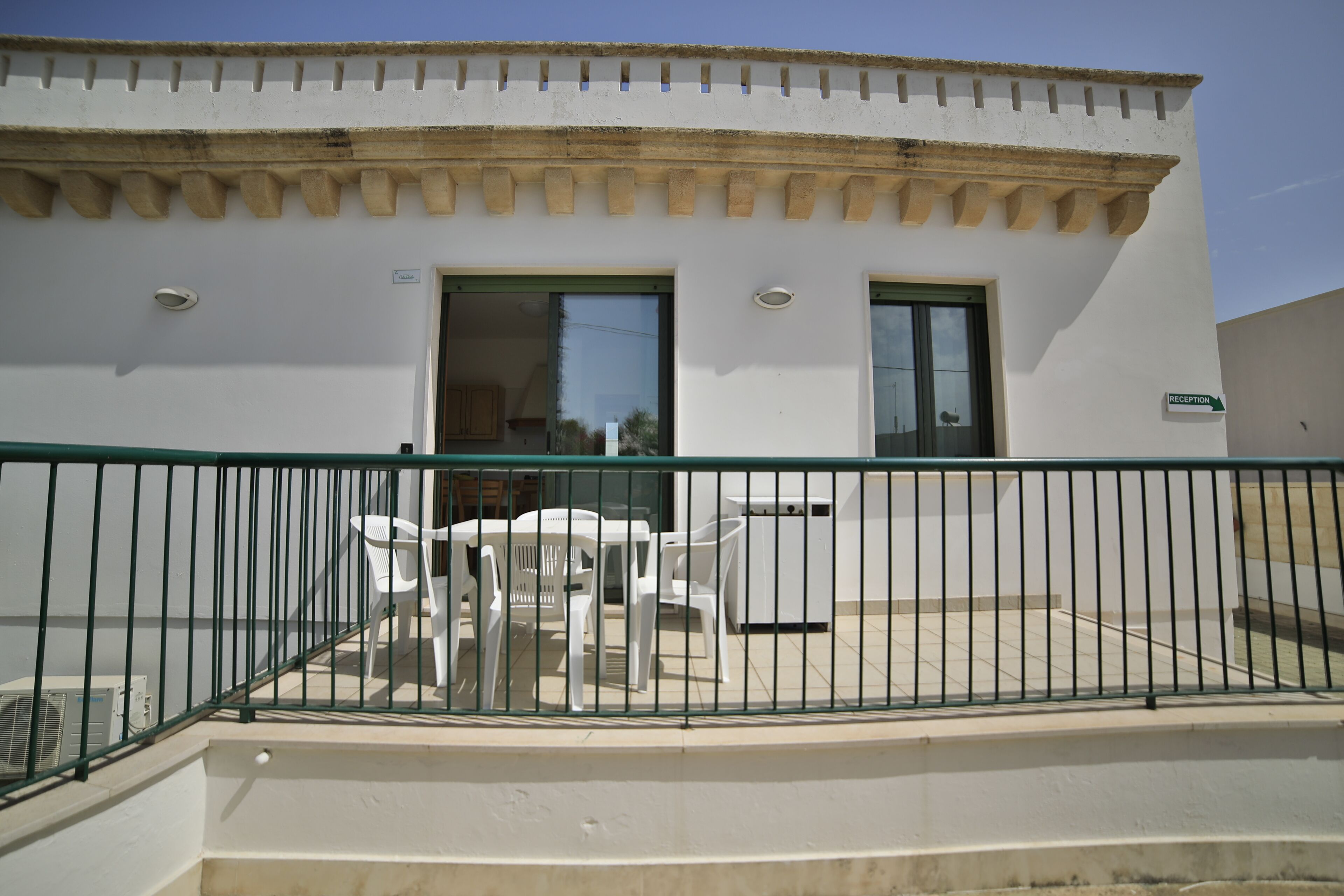 A building with a reception area, outdoor seating with white plastic chairs, and a metal railing.