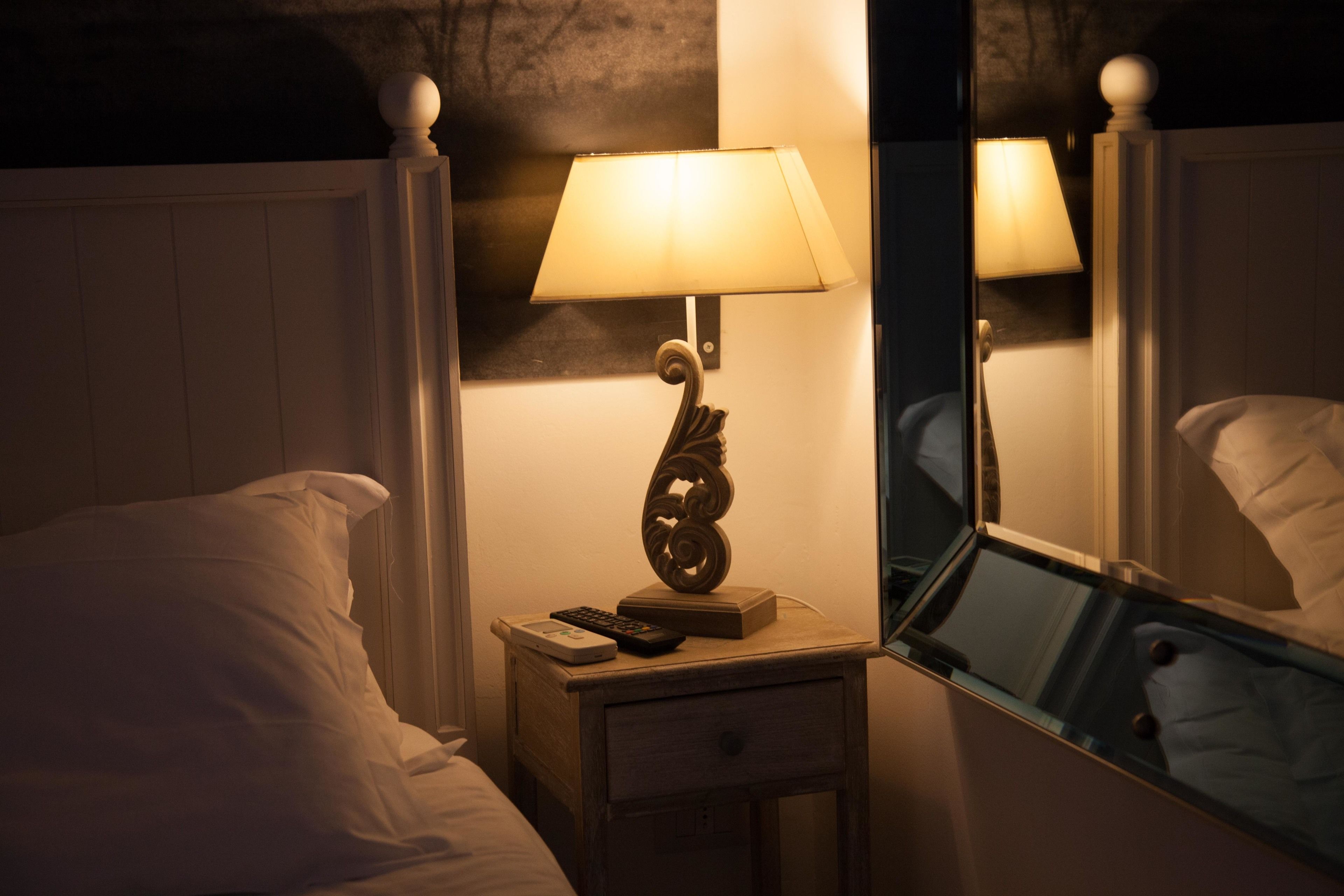 Un lit bien fait, avec du linge de lit blanc, une table de chevet avec une lampe, une télécommande et un petit livre.