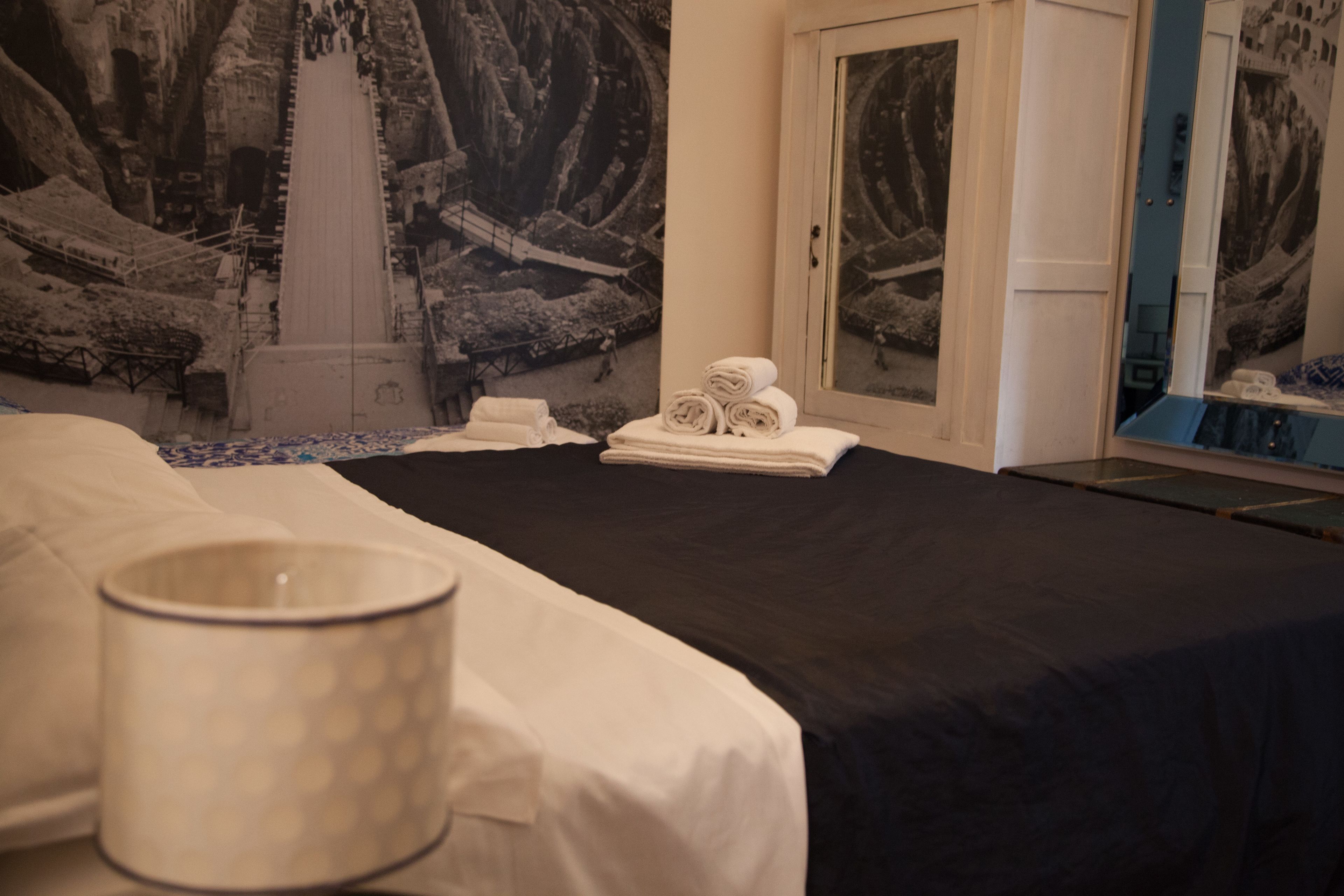 Une chambre d’hôtel avec un lit, une table de chevet, une lampe et un mur orné d’une grande fresque.
