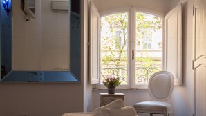 A bedroom with a bed, a chair, a window with a view of a building, and a small table with a plant. - White Vatican (Rome)