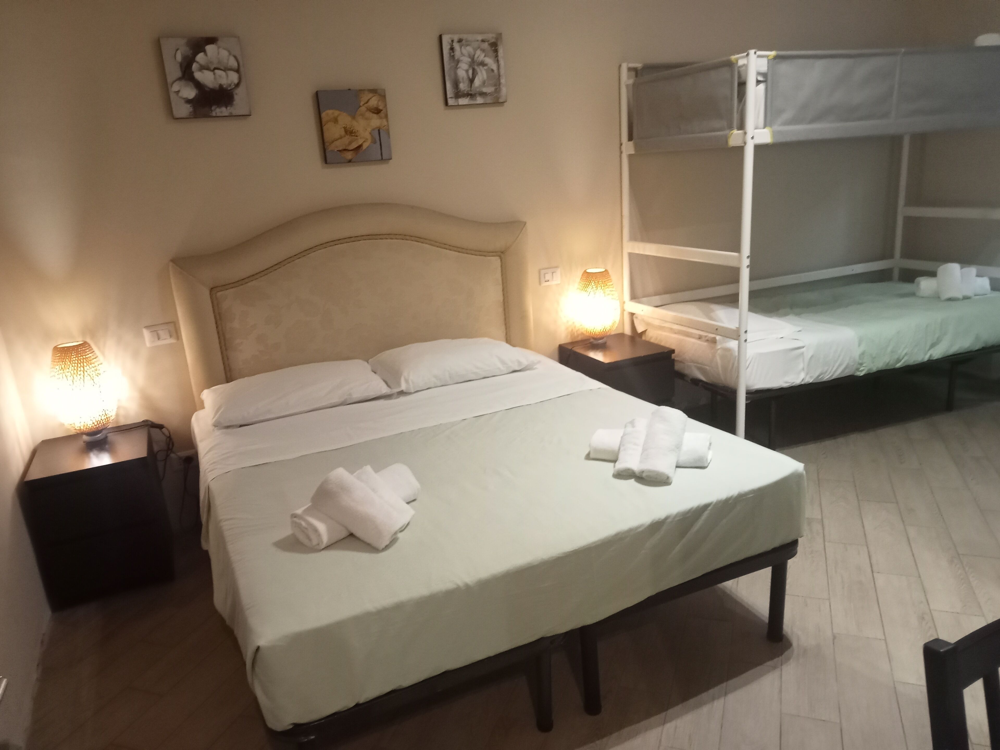 A hotel room with a large bed, a smaller bed, two bedside tables with lamps, and artwork on the walls.