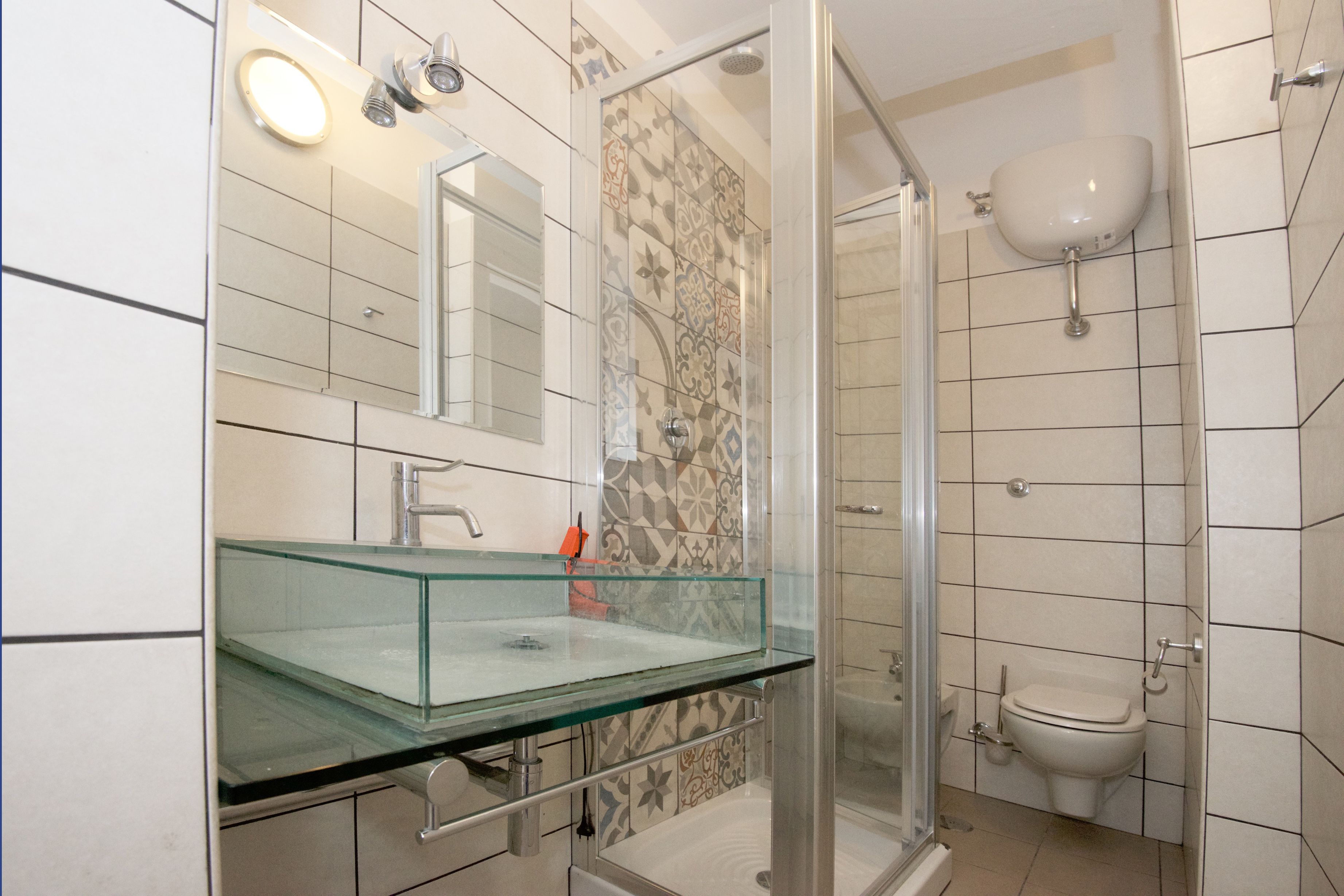A modern bathroom with a glass sink, a shower enclosure, and a toilet.